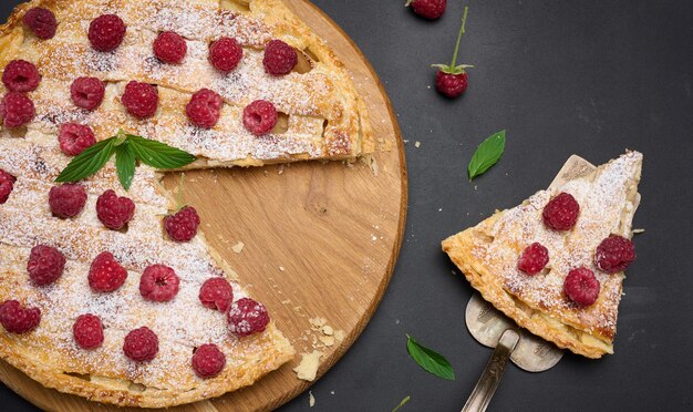round baked pie with apples and sprinkled with powdered sugar on a black table