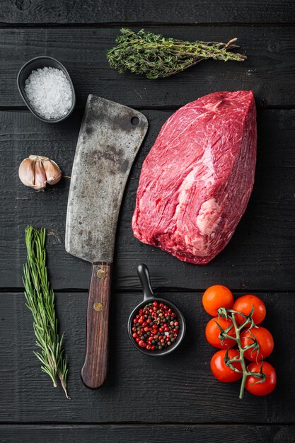 Round beef meat raw set with old butcher cleaver knife, on\
black wooden table, top view flat lay