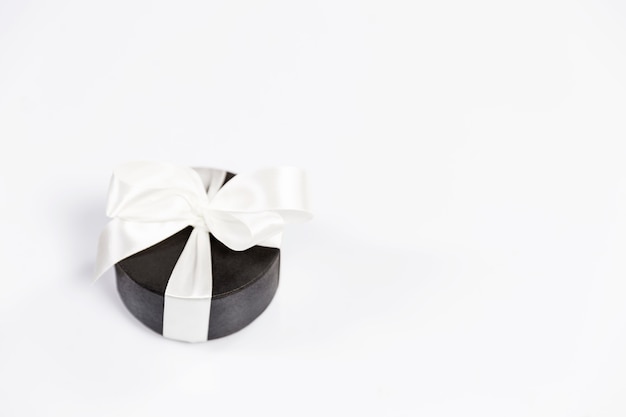 Round black gift box with a white bow on a white  background. Postcard. Space for text.