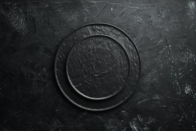 Round black stone plate on a black stone background top view\
free space for your text