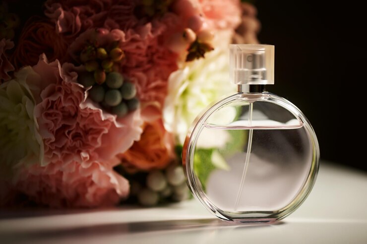 Photo a round bottle of perfume on a dark background near a bouquet with pink flowersaromatherapy and perfumes