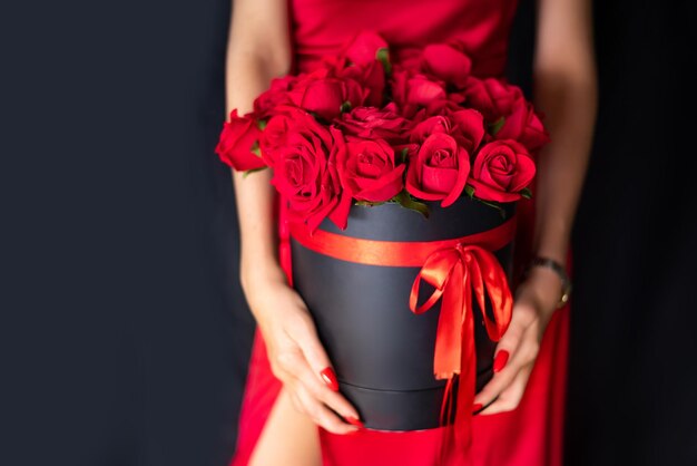 Photo round box with red roses on a black background in female hands