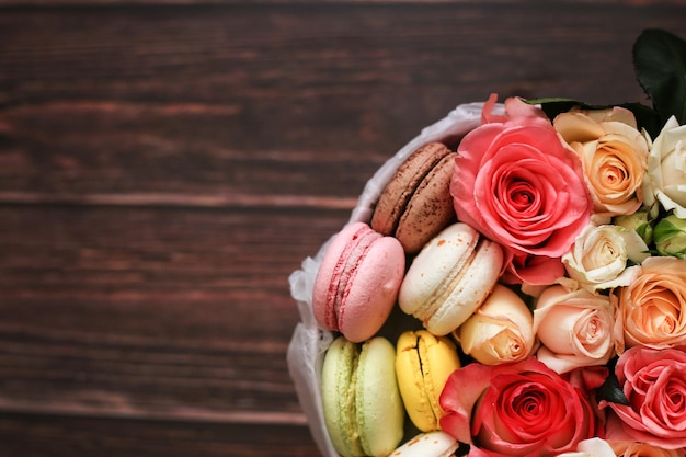 Round box with roses and cakes macaroons on wooden brown background Flowers in bloom Gift flowers