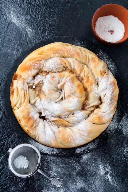 Round burek pie with an apple on a dark background. Traditional Serbian cuisine. Selective focus. Top view.