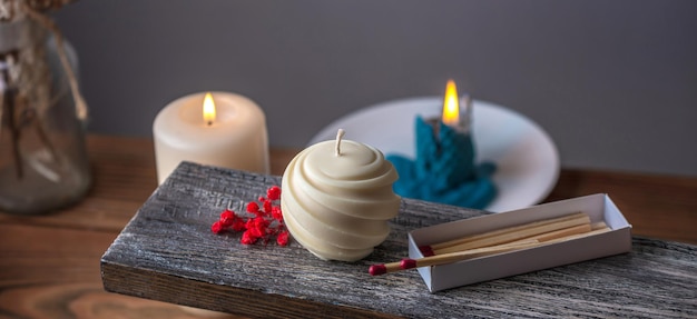 Round carved handmade candle and matches and red flowers on a wooden stand against the background of other lighted candles at the back