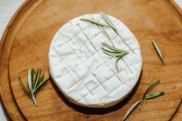 Round cheese in camembert mold with a sprig of rosemary on the table