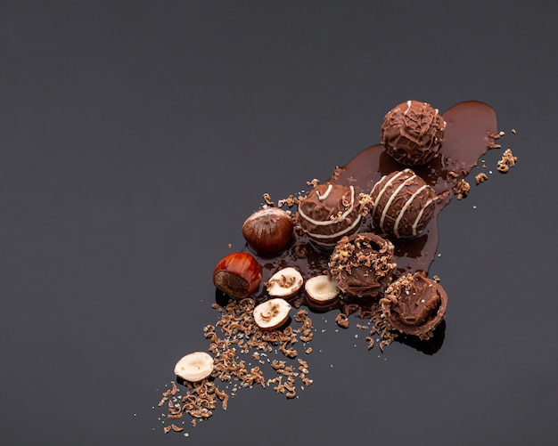 Round chocolate candies with a soft filling scattered in the lower right corner with chocolate chips nuts and mint leaves on a dark chocolate background with reflection The upper left corner is empt