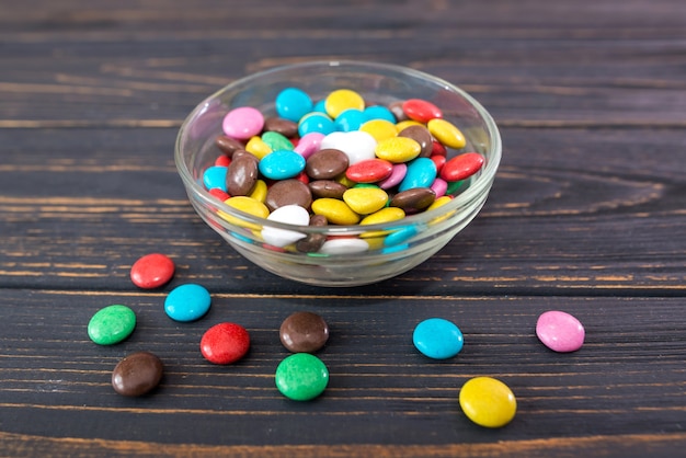 Round colored candies in a glass plate on a wooden background.