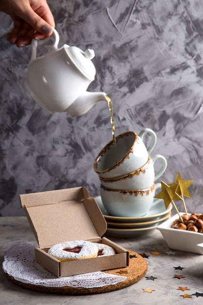 Round cookies with jam in the shape of a heart in a gift box among Christmas decorations and stars on a gray background