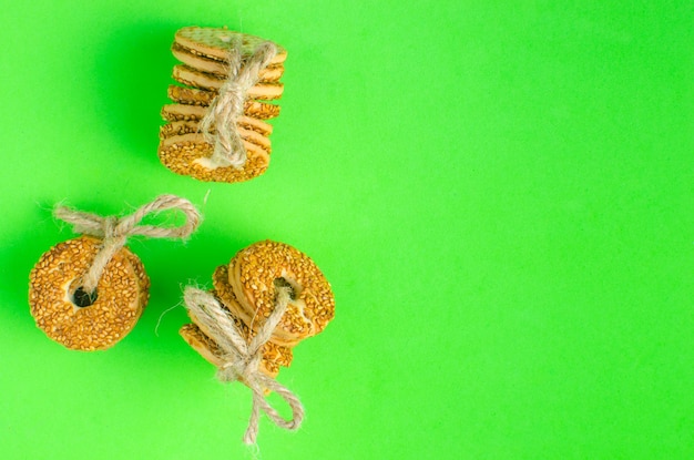 Round cookies with sesame seeds bound with a rope on a green background