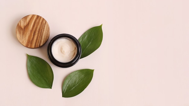 Round cosmetic cream container on the beige background,fresh juicy green leafs around.Organic cosmetics concept.Flat lay style,copy space,large banner.