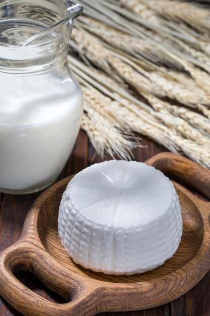 Round cottage cheese in a bowl with milk on a wooden table.