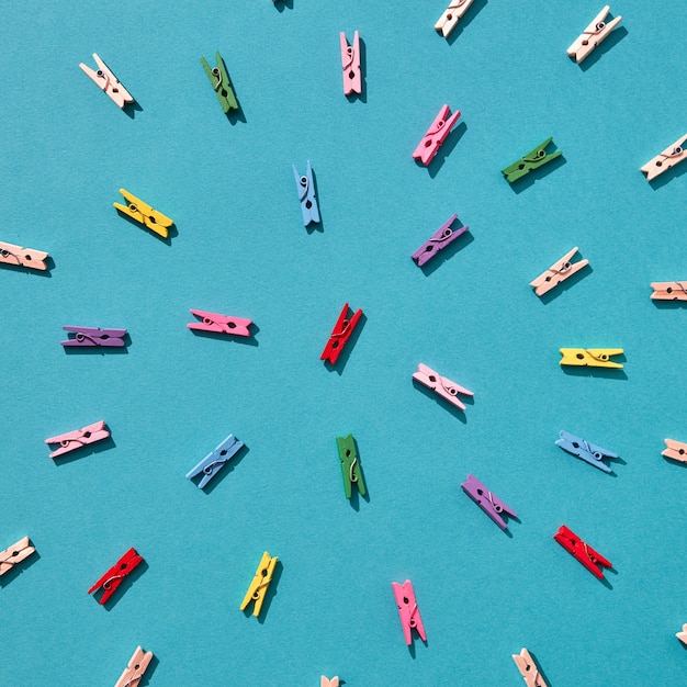 Round creative pattern from multicolored clothes pegs on a blue with hard shadows. Top view.