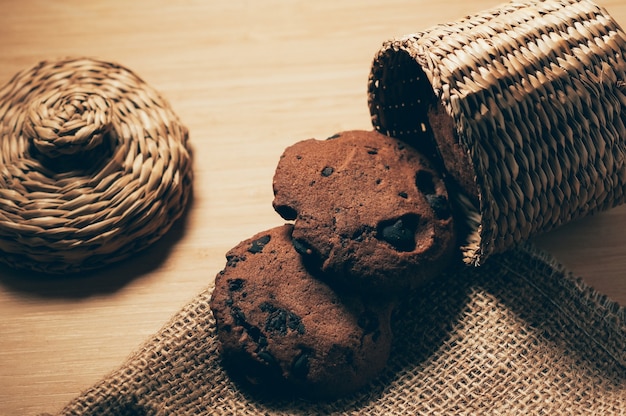 Biscotti rotondi croccanti al cioccolato con scaglie di cacao su tela ruvida e sfondo di cesto di vimini