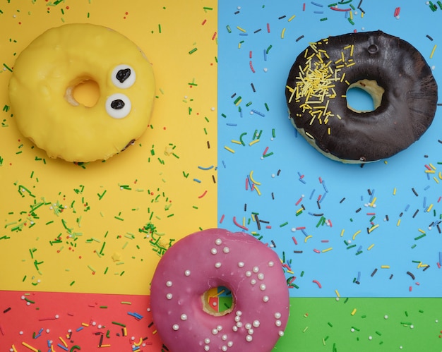 Round different donuts with sprinkles on a bright multi-colored background