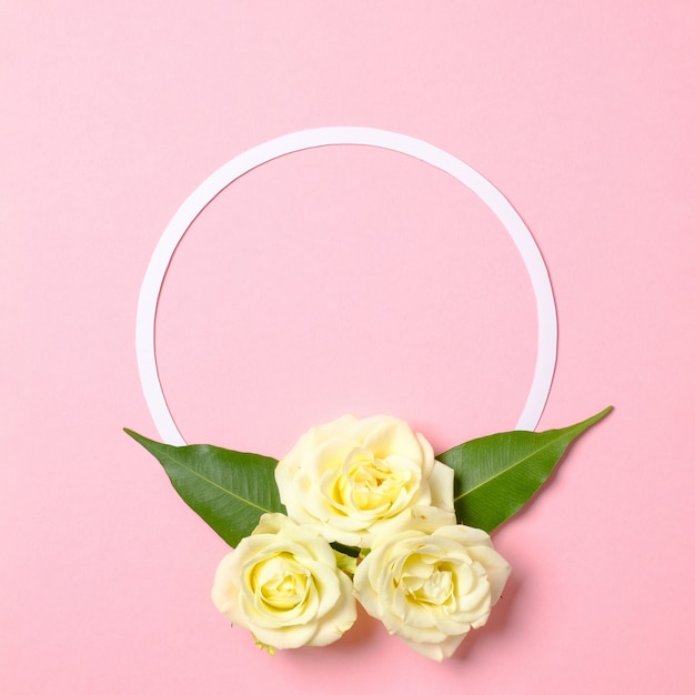 Round floral frame with roses flowers petals on pastel pink background.