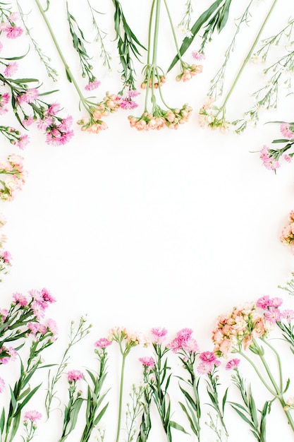 Round frame of colorful wildflowers, green leaves, branches on white