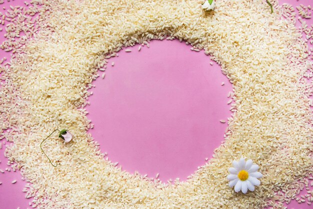 Round frame from dry white rice on pink background flat lay top view copy space