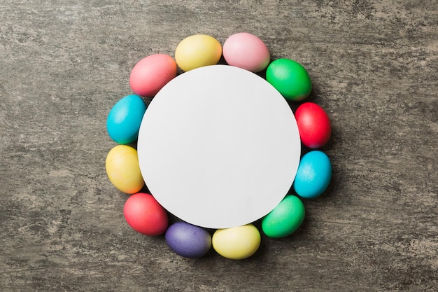 Round frame multicolored Easter eggs with white blank paper on a brown background closeup space for text blank for design selective focus tinted image