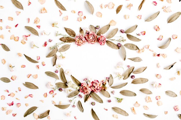 Round frame wreath pattern with roses, pink flower buds, branches and dried leaves isolated on white surface