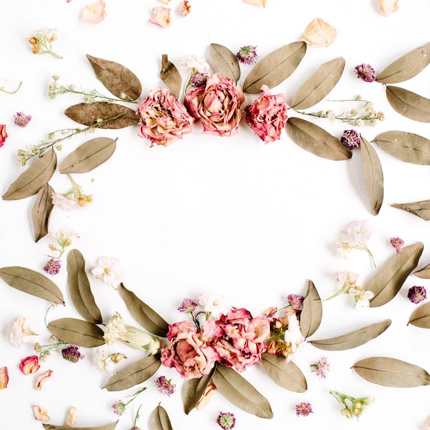 Round frame wreath pattern with roses, pink flower buds, branches and dried leaves isolated on white surface