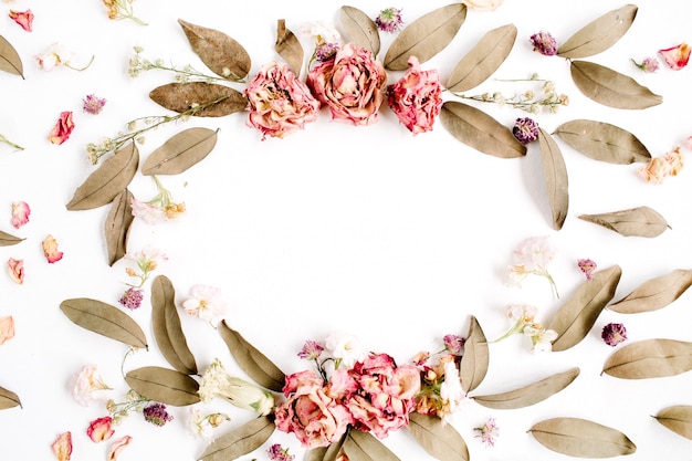 round frame wreath pattern with roses, pink flower buds, branches and dried leaves isolated on white surface