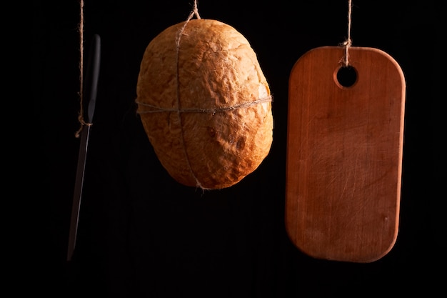 Round fresh bread hanging on a rope on a black background.