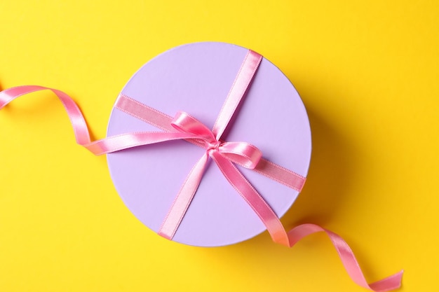 Round gift box with bow on yellow background