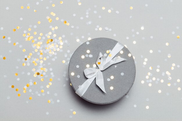 Round gift box with white ribbon bow top view confetti festive background