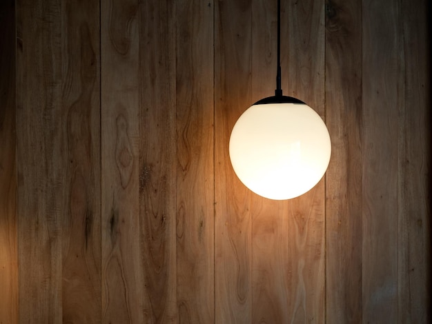 Round hanging lamp full moon shape with the light bulb inside shining in the wood wall background in the dark room with copy space