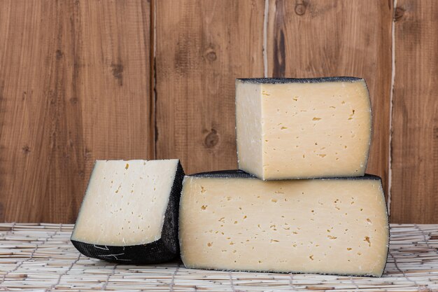 Round Head of hard cheese with small cut slice on wooden