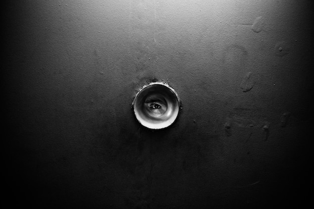 Round hole in the wall. An eye is visible through the hole. Someone is watching. Watching you and sniffing out your secrets.