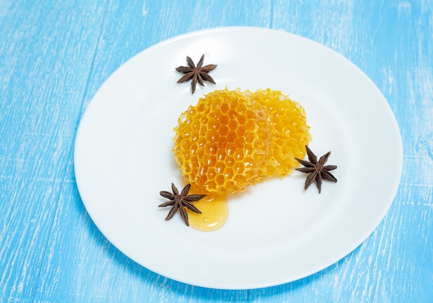 Round honeycombs and anise lie on a plate on a blue .