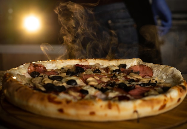 Round hot fresh pizza with steam lies on the table in the pizzeria. Food delivery.