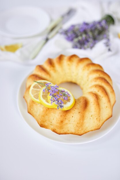 Round lemon cake on white table with lavender flower bouquet