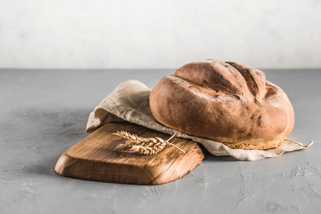 A round loaf of bread on a wooden Board with a grey linen napkin on a light background.