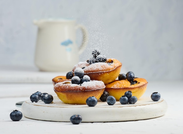 Round mini cottage cheese pies with blueberries on a white wooden board delicious sweet dessert