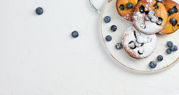 Round mini cottage cheese pies with blueberries on a white wooden board