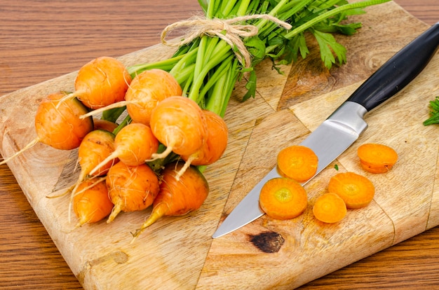 Round orange carrot on wooden board with knife.