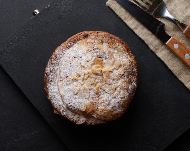 Round pastry with almonds and butter sprinkled with powdered sugar on the table puff pastry