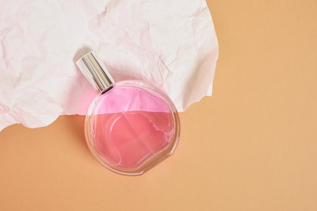 Round perfume bottle with a silver cap on a background of white crumpled paper, pink perfume in a transparent glass packaging, mock up a simple shape of a perfume bottle