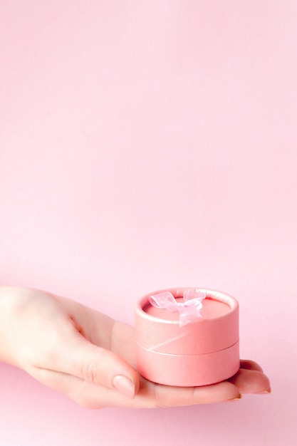 Round pink gift box in women's hands on a pink background. Festive concept for Valentine's day, Mother's day or birthday