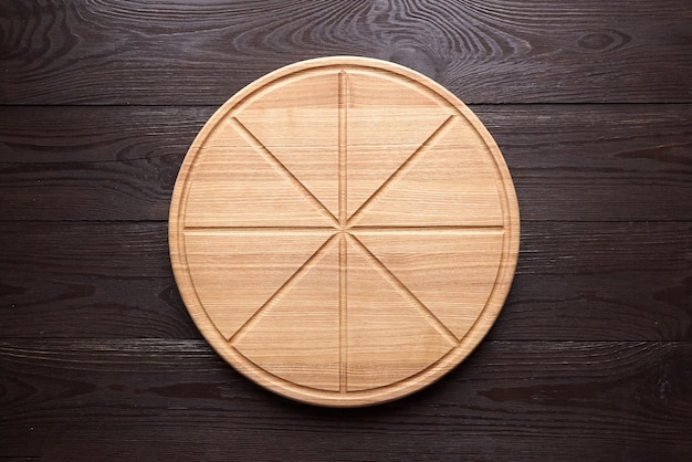 Photo round pizza cutting board with slice grooves on brown wooden table top view