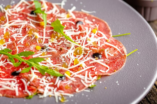 round plate, appetizer Stroganina from marbled beef with goat cheese and caviar, cold cuts