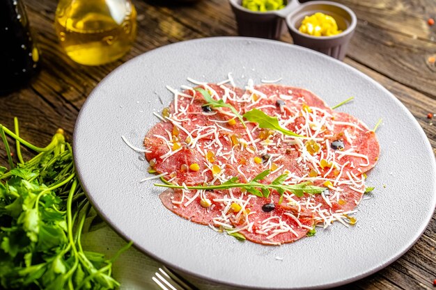 Foto piatto tondo, antipasto stroganina di manzo marmorizzato con caprino e caviale, salumi