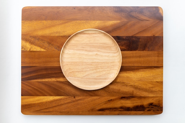 Round plates made of rubber wood with natural colors, polished and lacquered, placed on a wooden chopping block made of Chamchuri or mimosa trees with a white background.