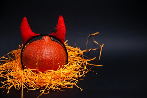 Round pumpkin with devil horns and a crawling spider standing on orange straw