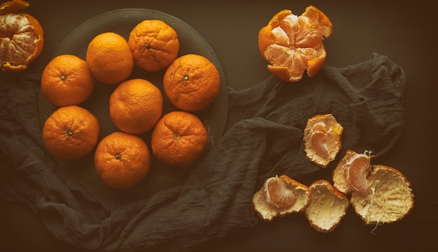 Round ripe tangerines in a plate on a black textile napkin, top view