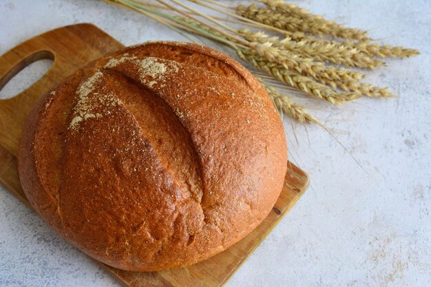 круглый ржаной хлеб, изолированный на разделочной доске и украшенный колосьями пшеницы, макрос