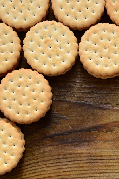 A round sandwich cookie with coconut filling lies in large quantities on a brown wooden surface